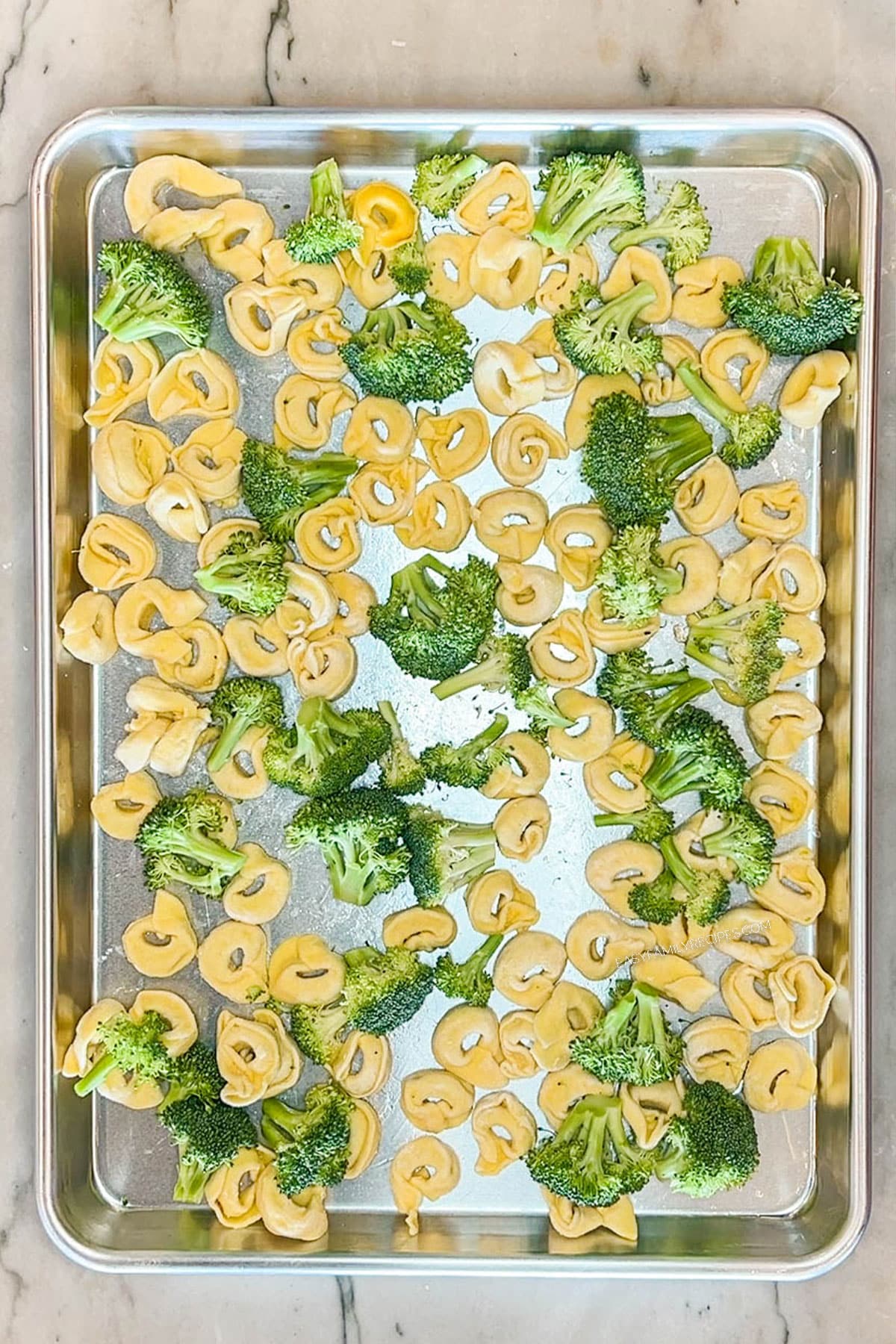 Step 1 to make Sheet Pan Italian Sausage Tortellini- broccoli and tortellini on baking pan