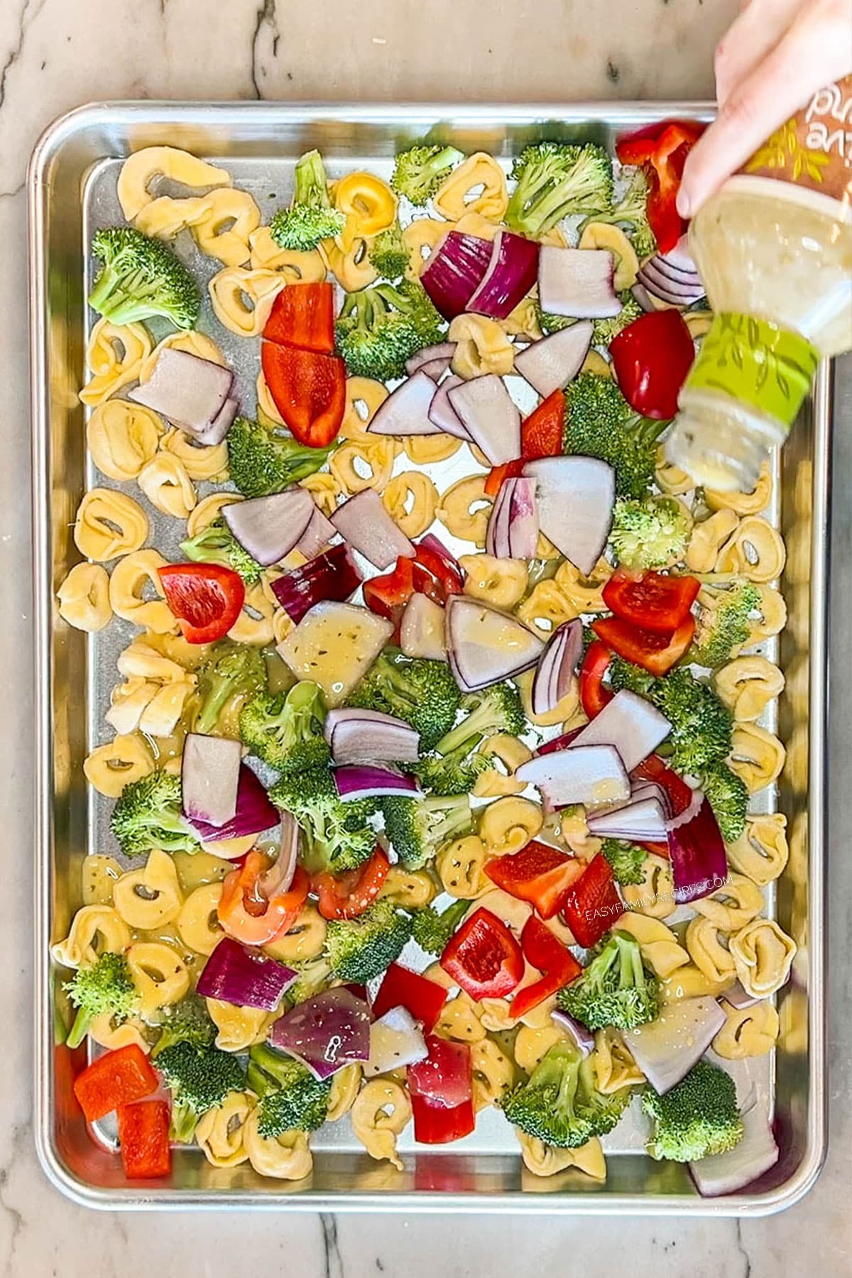 Step 2 to make Sheet Pan Italian Sausage Tortellini- Broccoli, tortellini, red peppers and red onions on baking pan