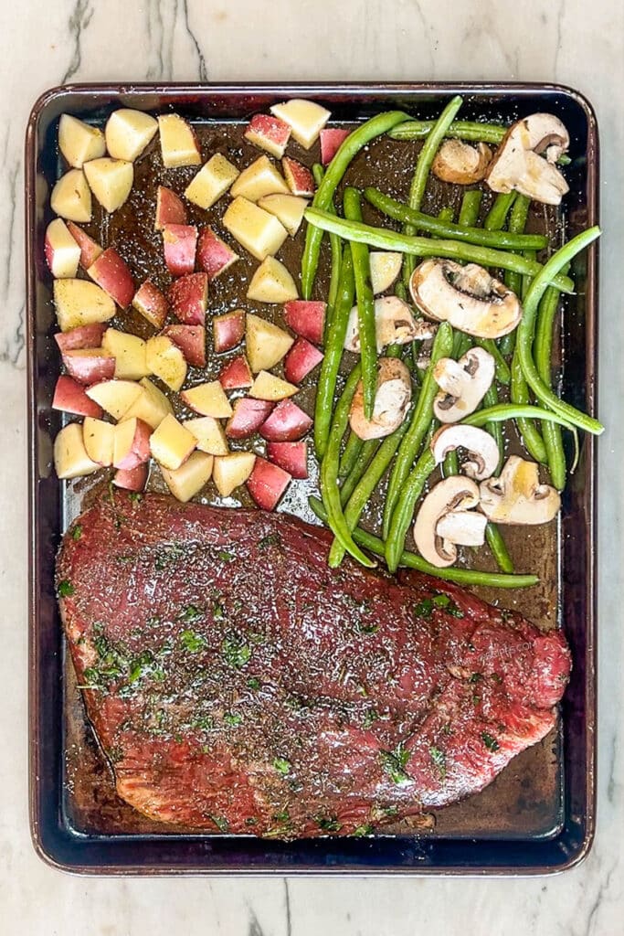 uncooked steak and veggies on a sheet pan.