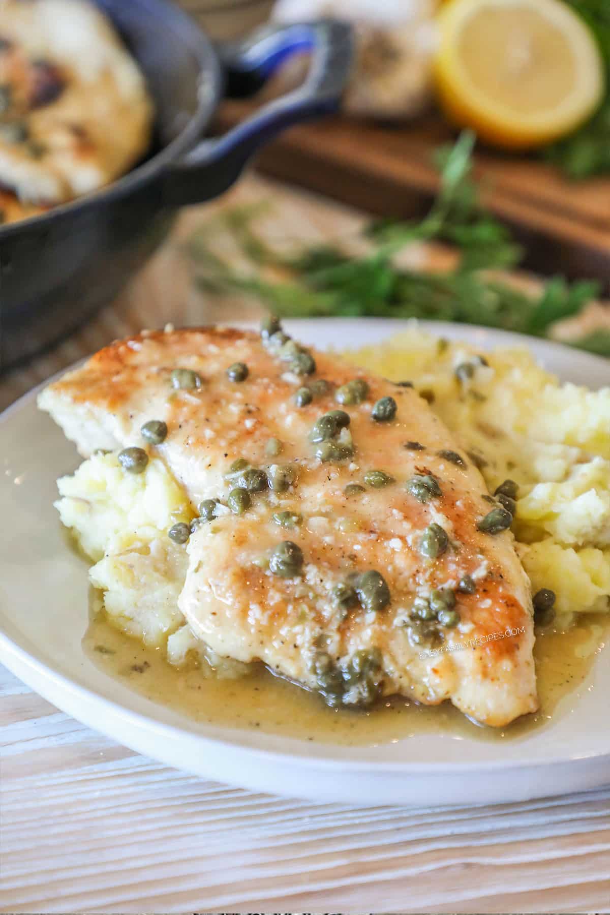 Chicken piccata served on a plate over a bed of mashed potatoes.