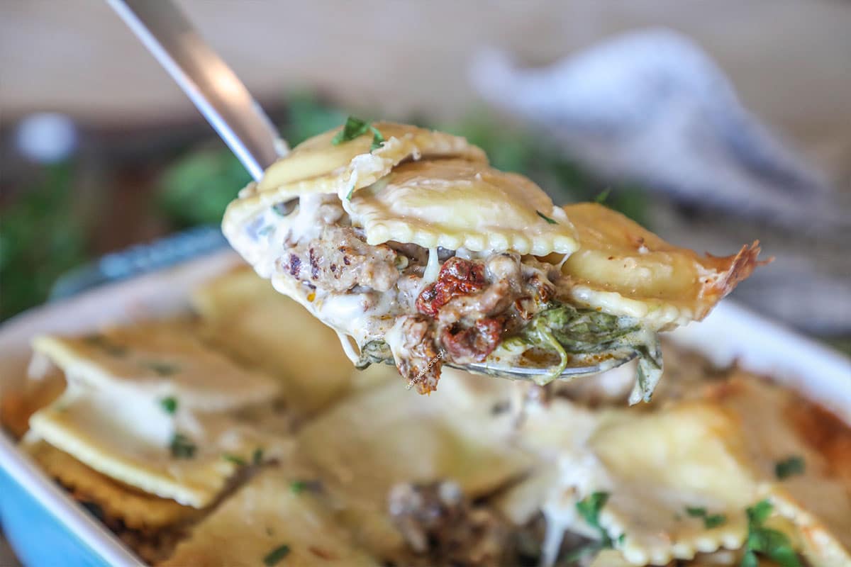 Marry Me Ravioli Casserole in blue baking pan with spoon lifting out