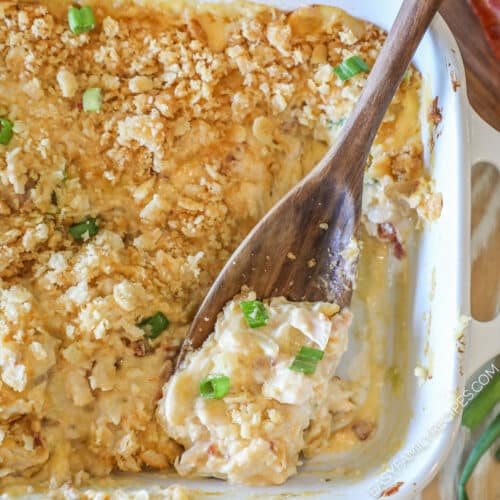 Top down view of Neiman Marcus Chicken Casserole in white baking dish with wooden spoon lifting out