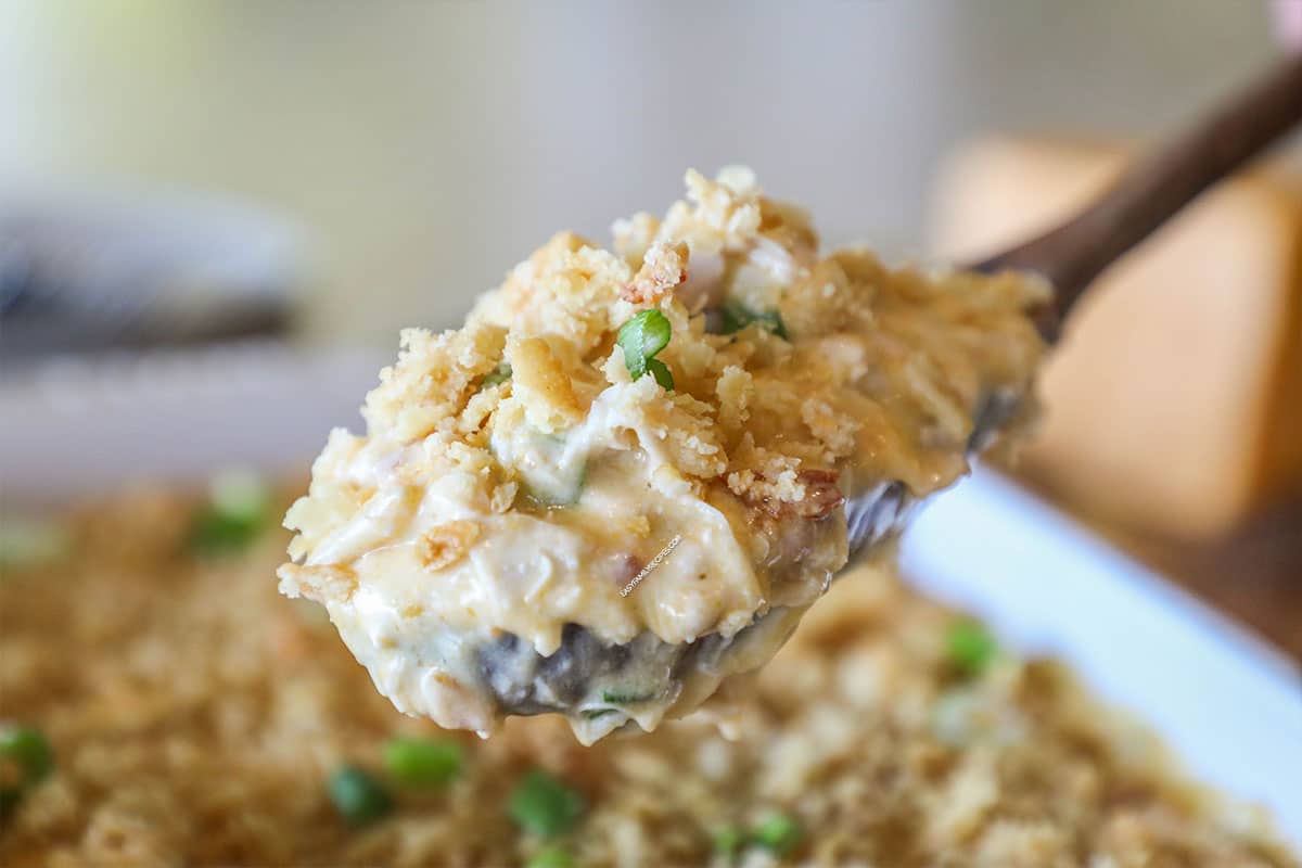 Neiman Marcus Chicken Casserole in white baking dish with wooden spoon lifting out