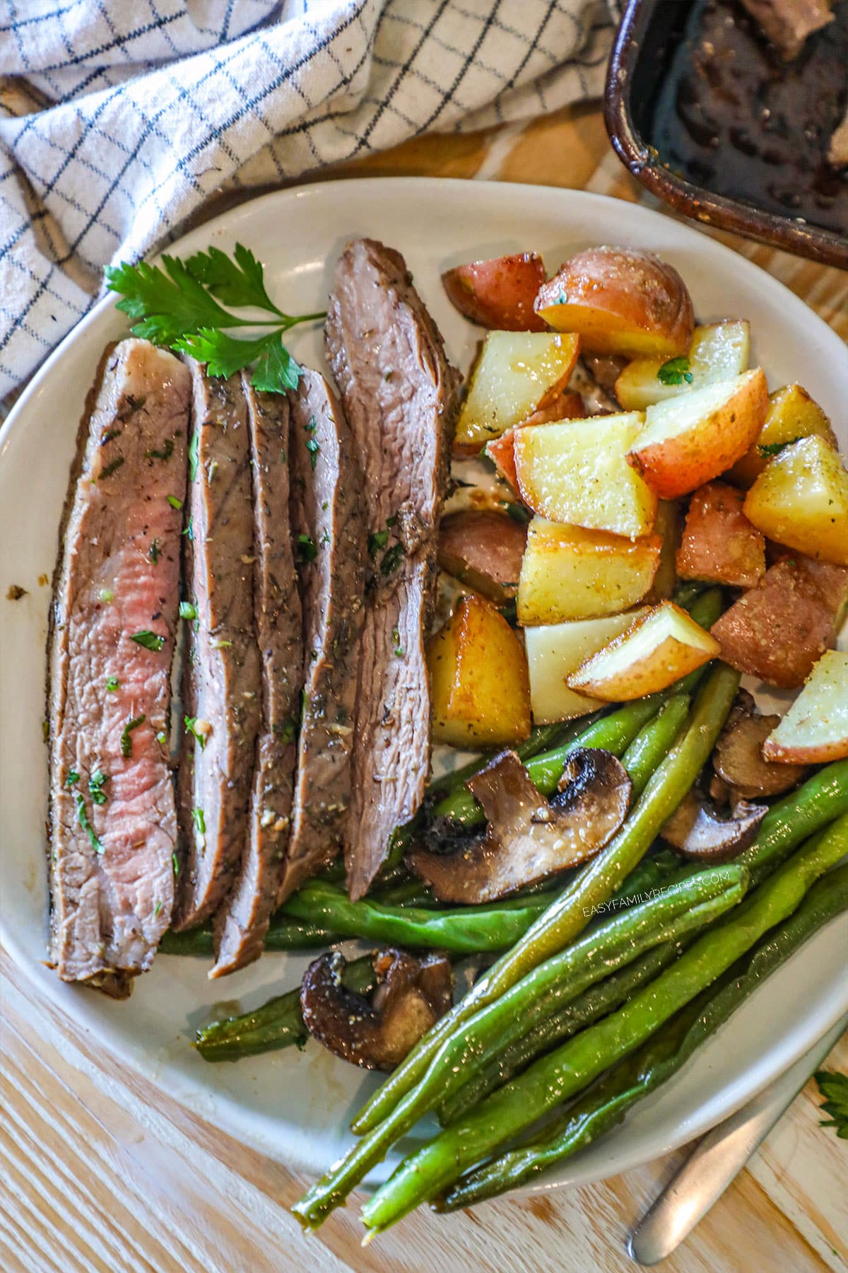 above image of a plate with sliced steak, roasted green beans, potatoes, and mushrooms.