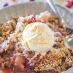 Close up of a scoop of ice cream on some apple cranberry crumble in a bowl.