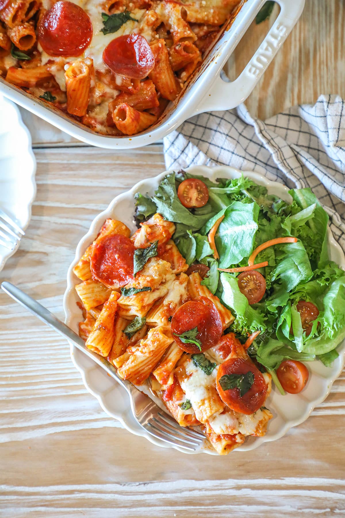 Baked pepperoni rigatoni with hot honey drizzle served on a plate with a side salad.