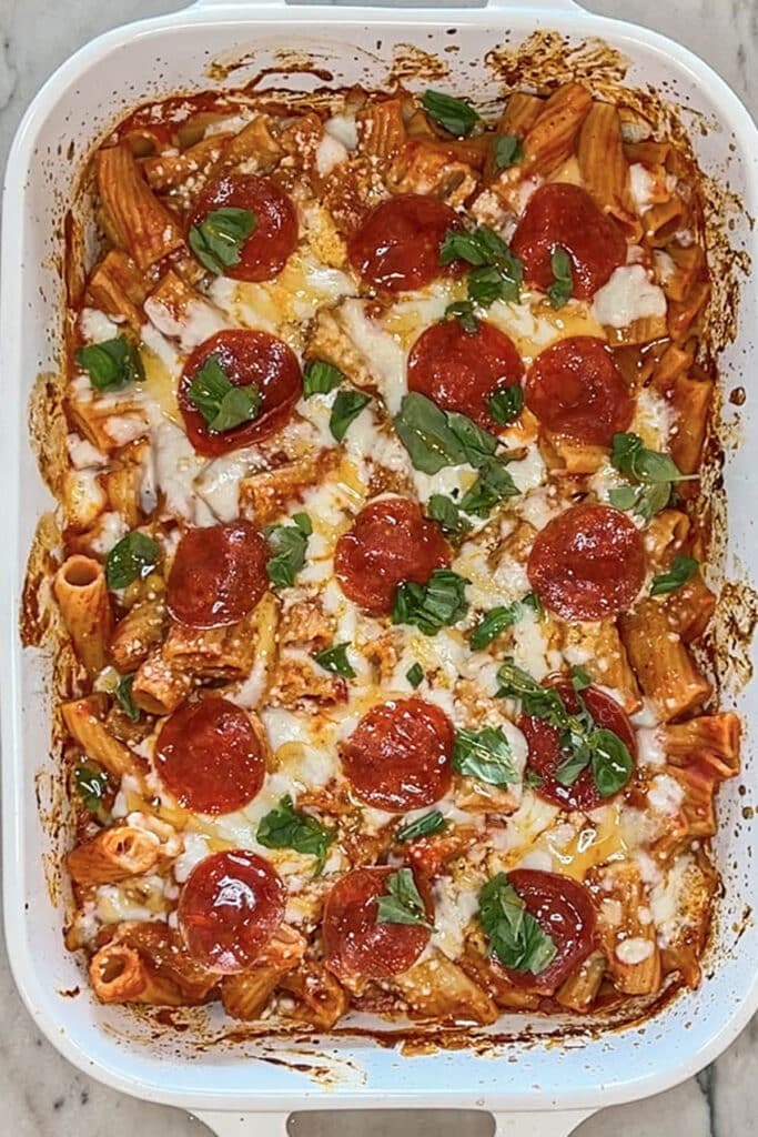 Finished pepperoni baked rigatoni being drizzled with hot honey in a baking dish.