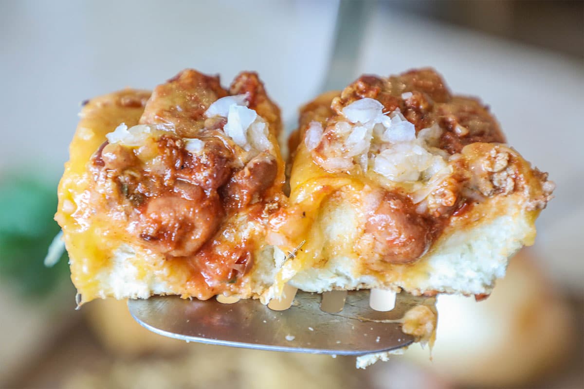 Close up of two Chili Dog Sliders being lifted by a spatula