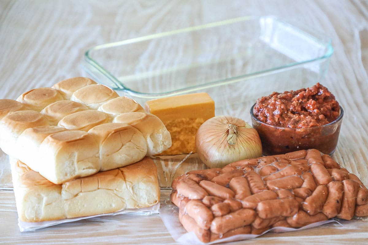 Ingredients needed to make Chili Dog Sliders- on a wooden background and with a clear 9x13 pan