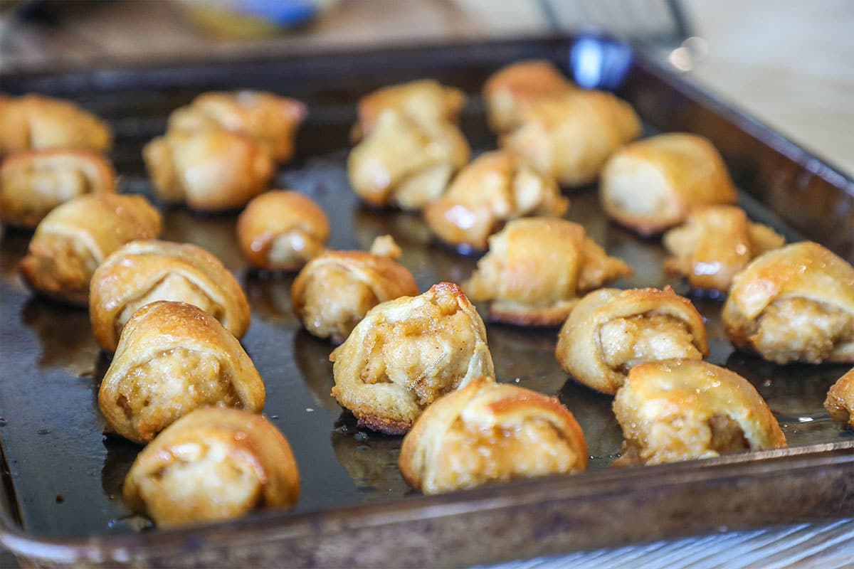 Close up of cooked Chicks in a Blanket, lined on a sheet pan. On a wooden background