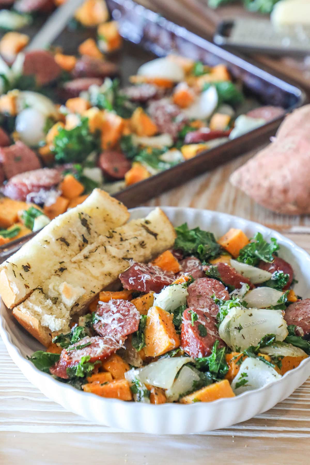 Bowl of sheet pan sausage and sweet potatoes with garlic bread.