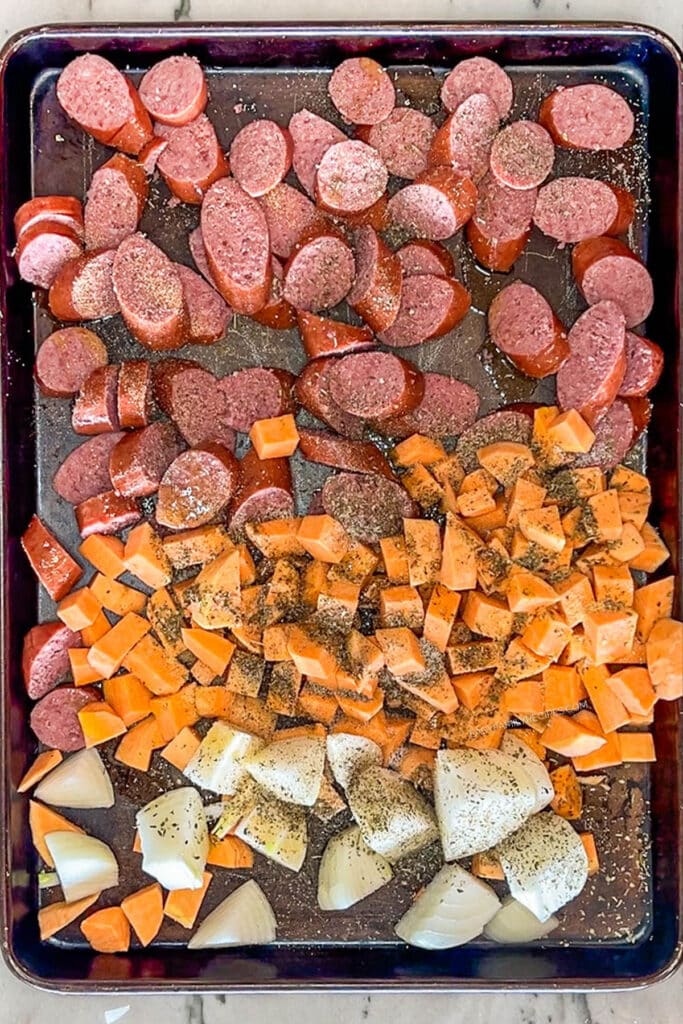 Seasonings added to pan of uncooked sausage, sweet potatoes, and onions.