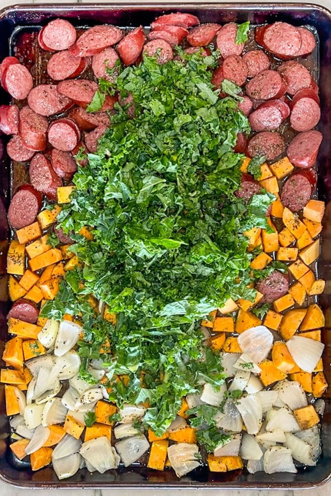 Kale added to sheet pan with sausage, sweet potatoes, and onions.