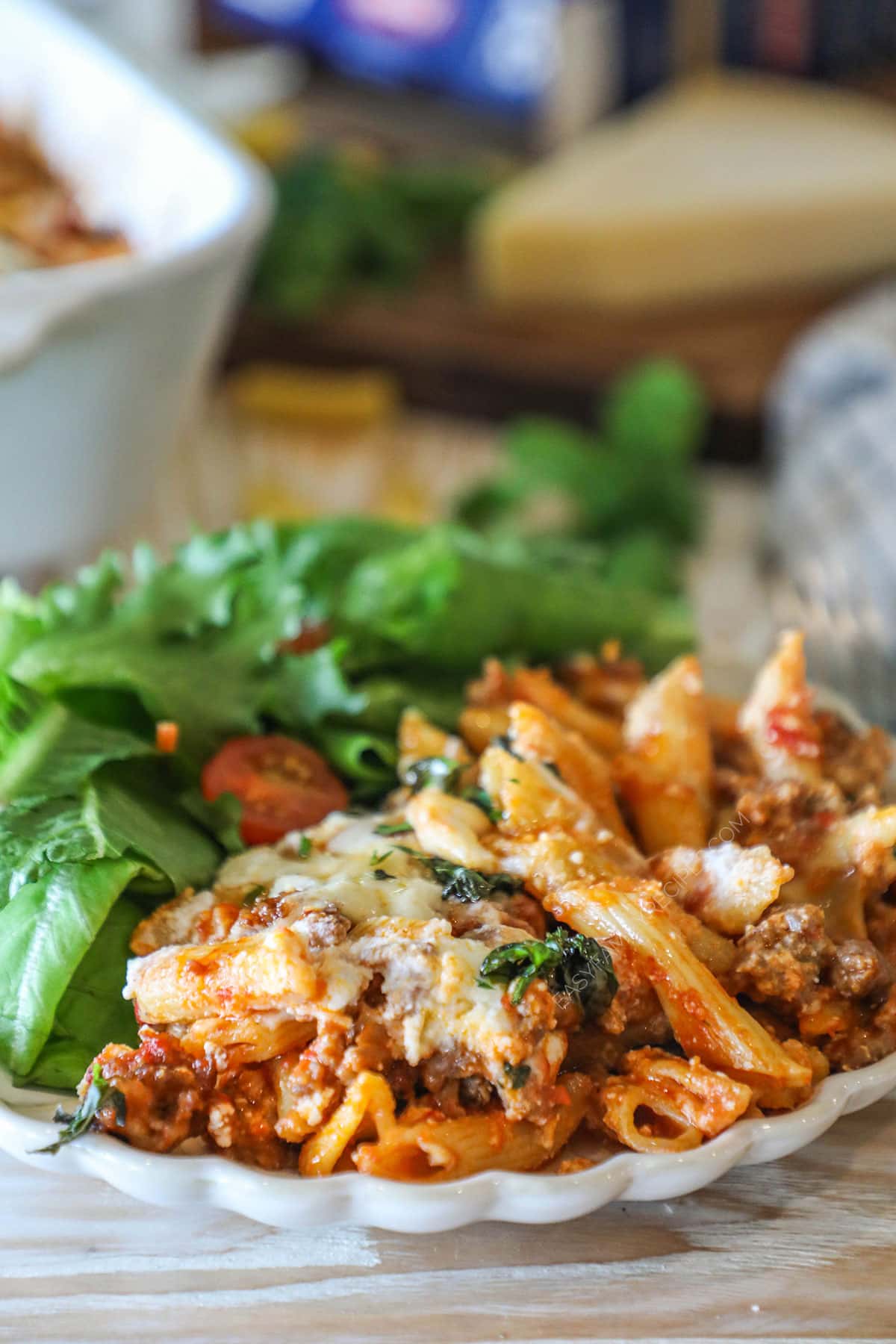 Side view of a portion of baked pepperoni rigatoni served on a plate with salad.
