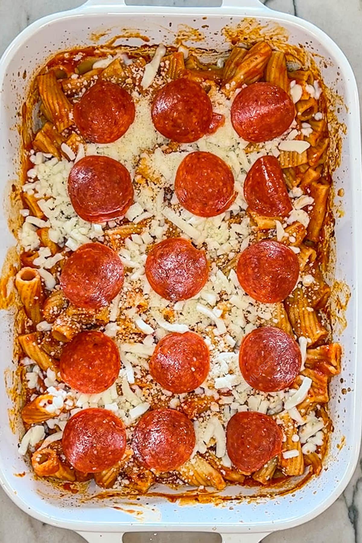 Pepperoni and cheese placed on top of baked pasta.