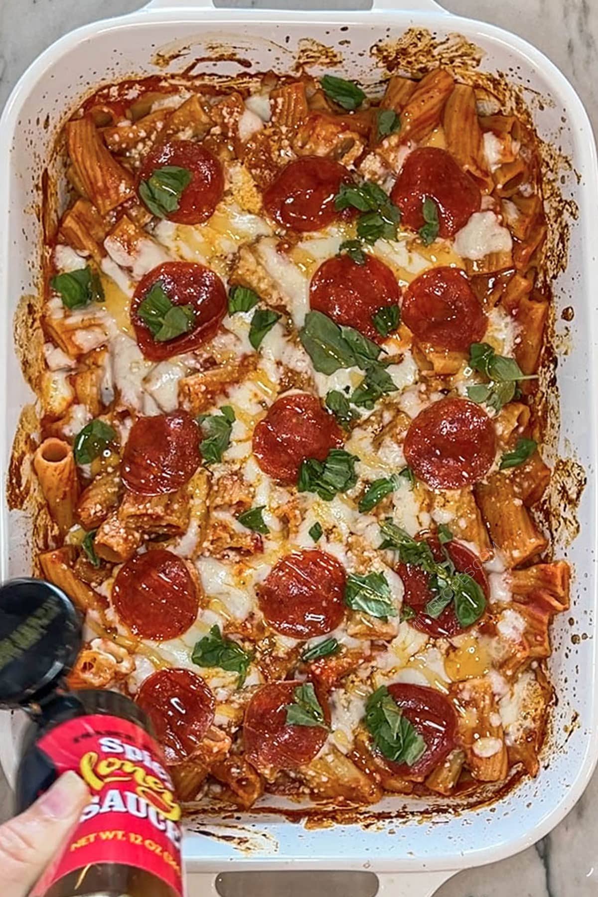 Finished pepperoni baked rigatoni being drizzled with hot honey in a baking dish.