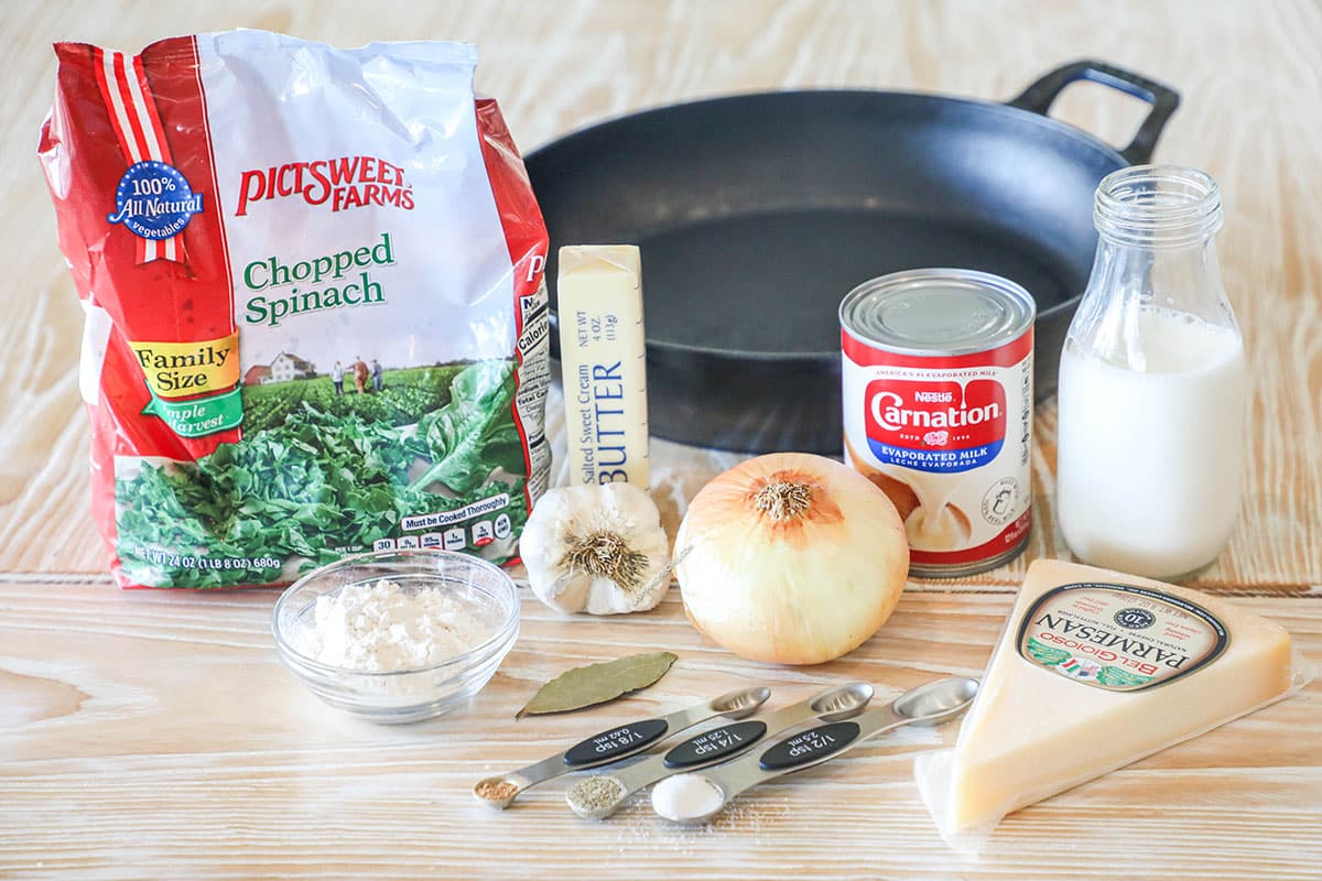 Ingredients for easy creamed spinach, including frozen spinach, butter, evaporated milk, Parmesan, bay leaf, flour, garlic, onion, milk, seasonings.