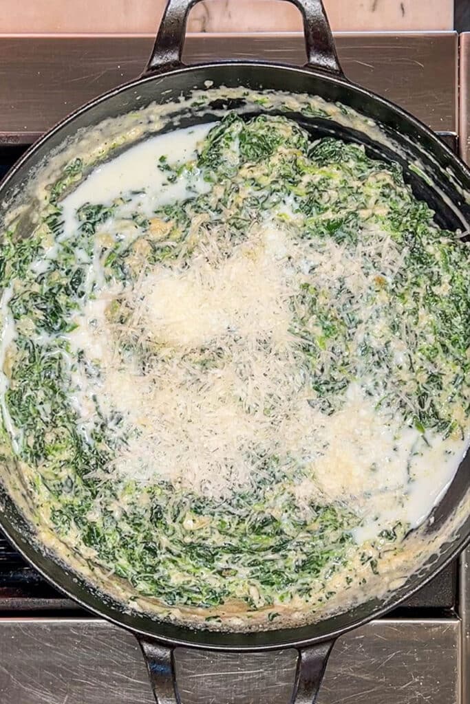 Shredded Parmesan cheese and milk added to pan of creamed spinach.