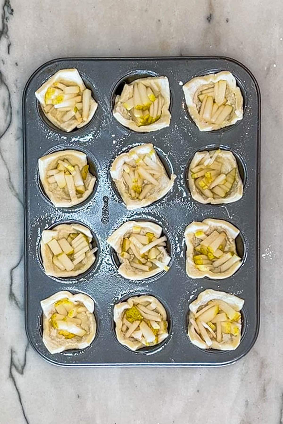 Step 4 for making Pear and Gorgonzola Puff Pastry Bites- fill muffin tins with diced pears