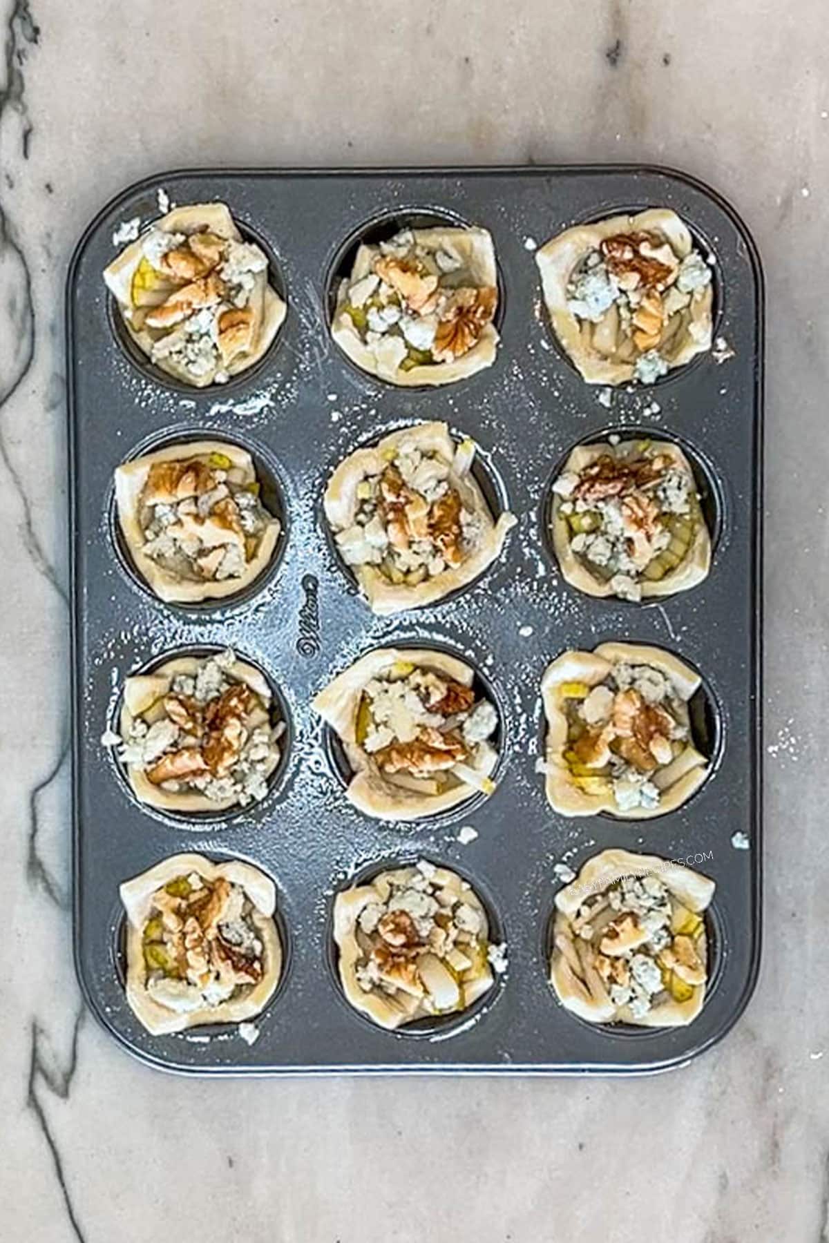 Step 5 for making Pear and Gorgonzola Puff Pastry Bites- add gorgonzola cheese and chopped walnuts to each tin