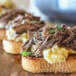 Slow cooker beef manhattan open faced sandwiches on wooden board.