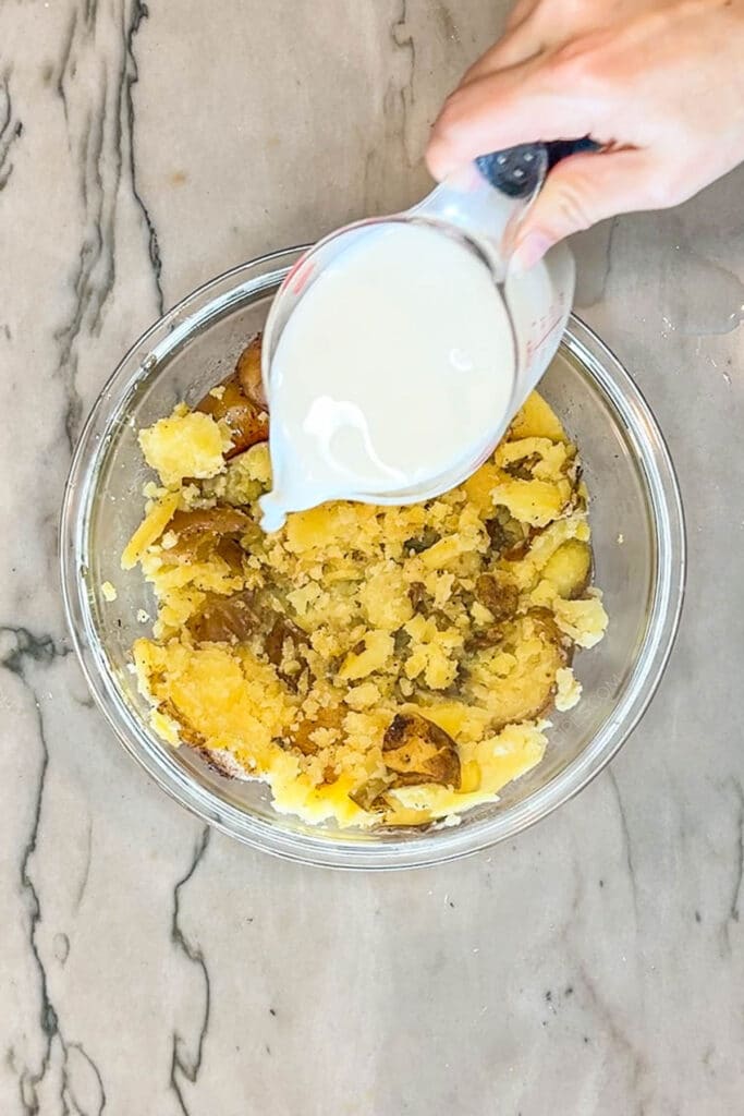 Pouring milk into bowl of potatoes.
